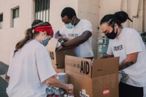 Volunteers with masks packing aid boxes with supplies outdoors during the day.